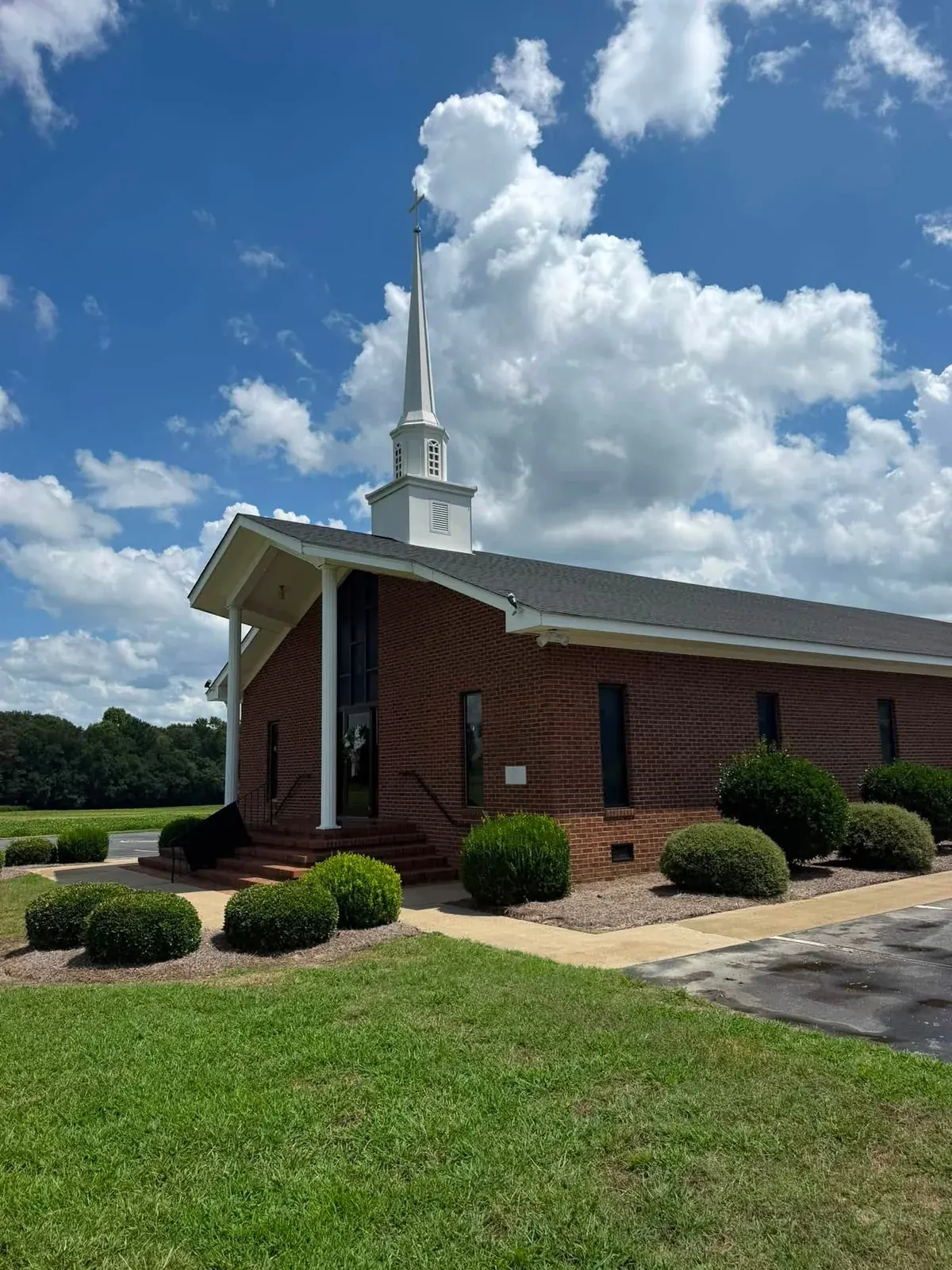 Side view of a brick church with a white steeple, columns, and surrounding walkways