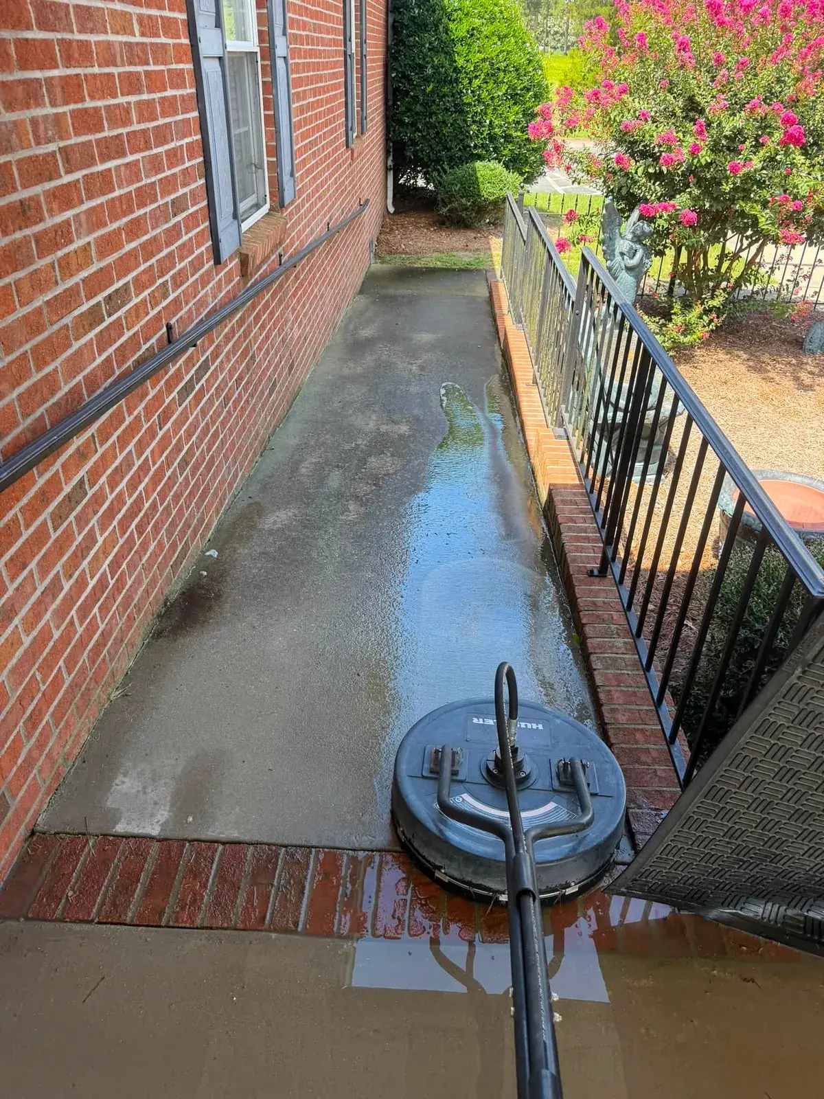 Surface cleaner running on a brick-bordered concrete walkway, half of it still dark with grime